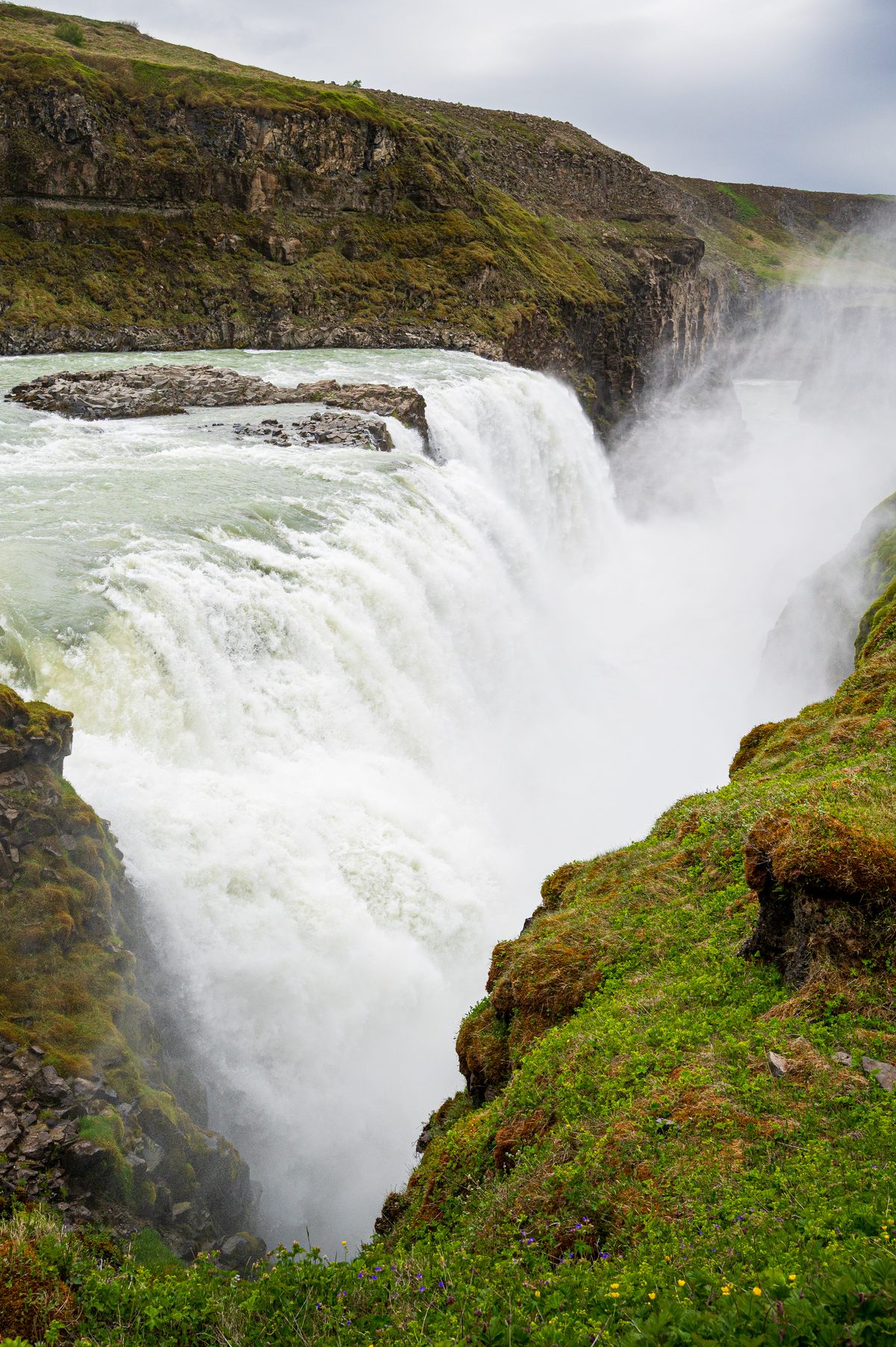 An immense volume of glacial water thunders over a rocky precipice into a steep canyon, sending thick clouds of mist high into the air.