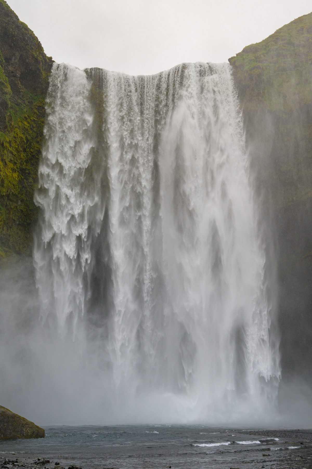 A close view captures the broad, powerful face of Skógafoss crashing into a mist-filled pool between mossy cliffs.