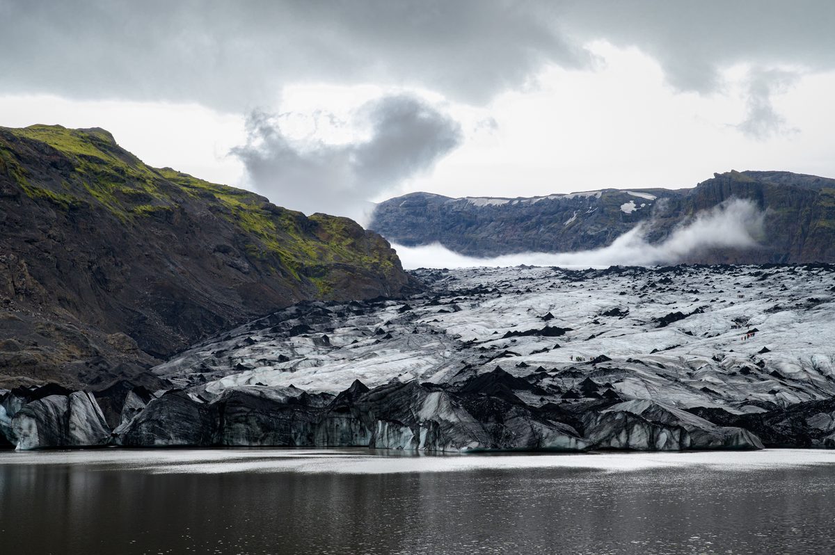 Crevassed, ash-streaked ice fills the valley at Sólheimajökull, with tiny glacier hikers revealing the immense scale of the frozen landscape.