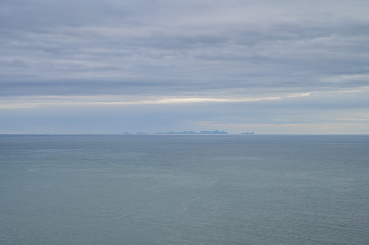 The low silhouettes of the Westman Islands hover along the distant horizon beyond a calm steel-blue sea.