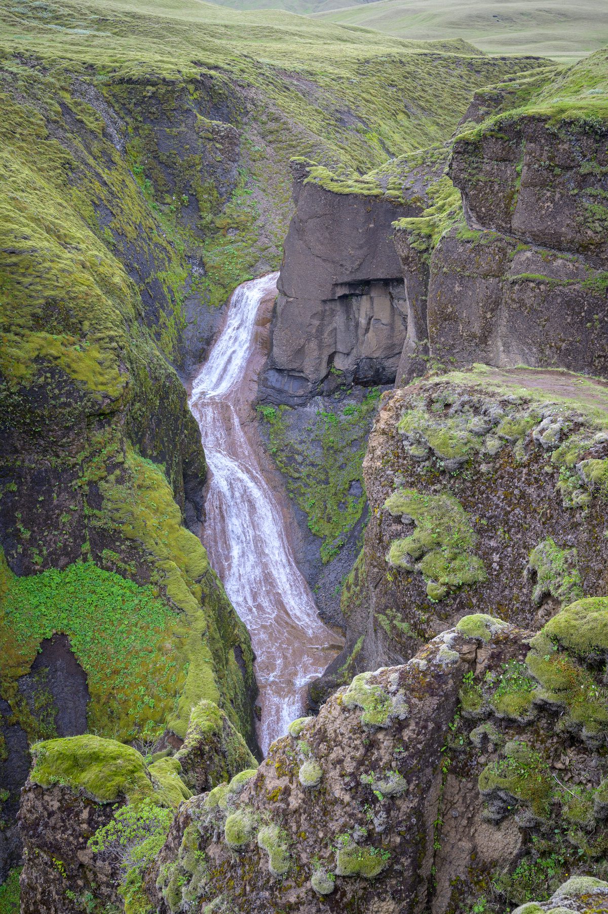 A slender waterfall slips through a narrow cleft in the canyon’s moss-covered volcanic walls.