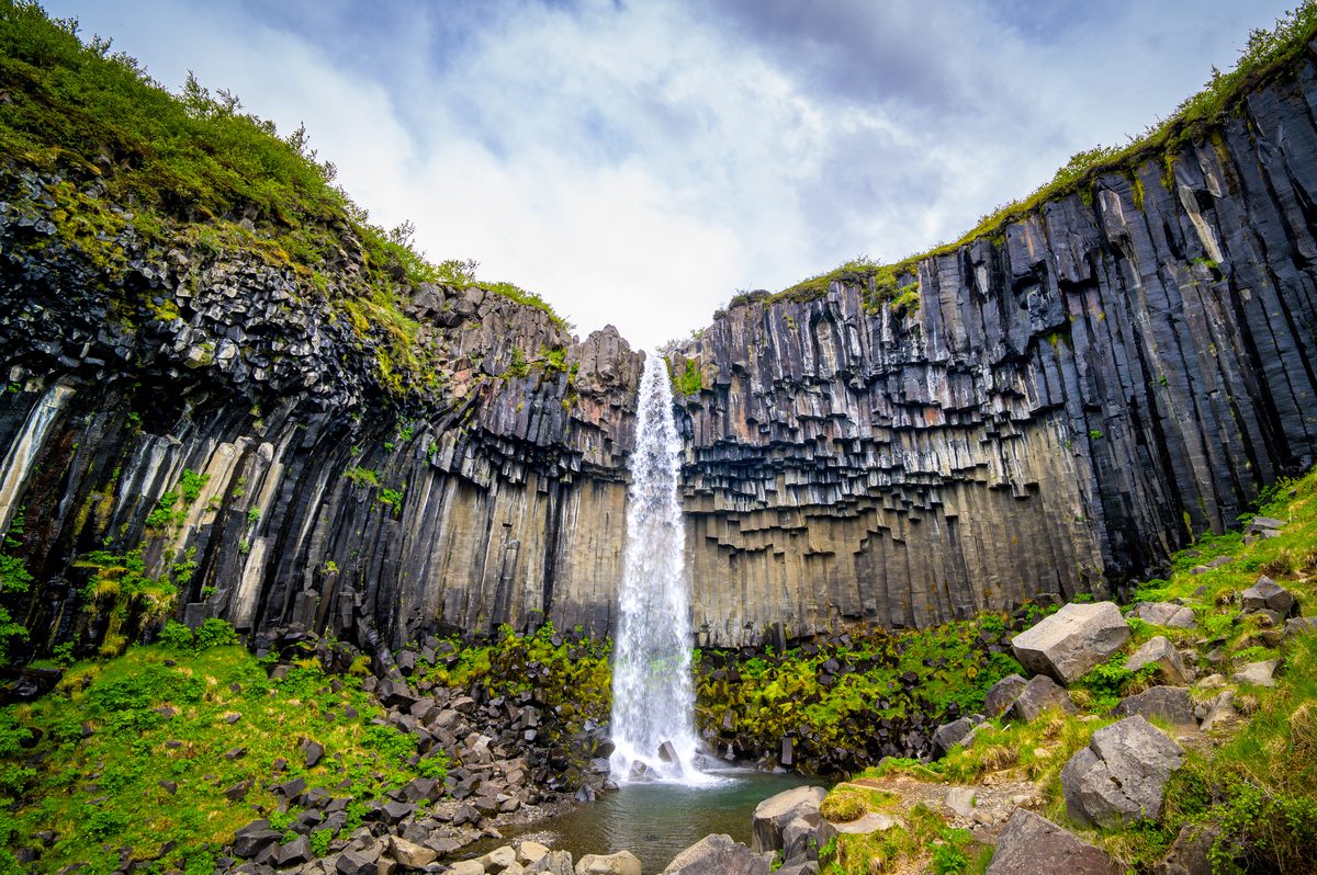 The slender white ribbon of Svartifoss drops into a rocky pool beneath towering columns of black basalt.