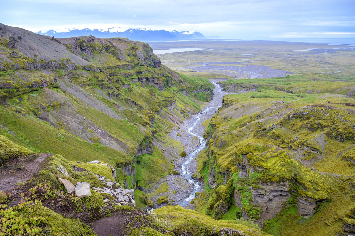 A narrow river threads through the green canyon toward the wide glacial plain beyond.