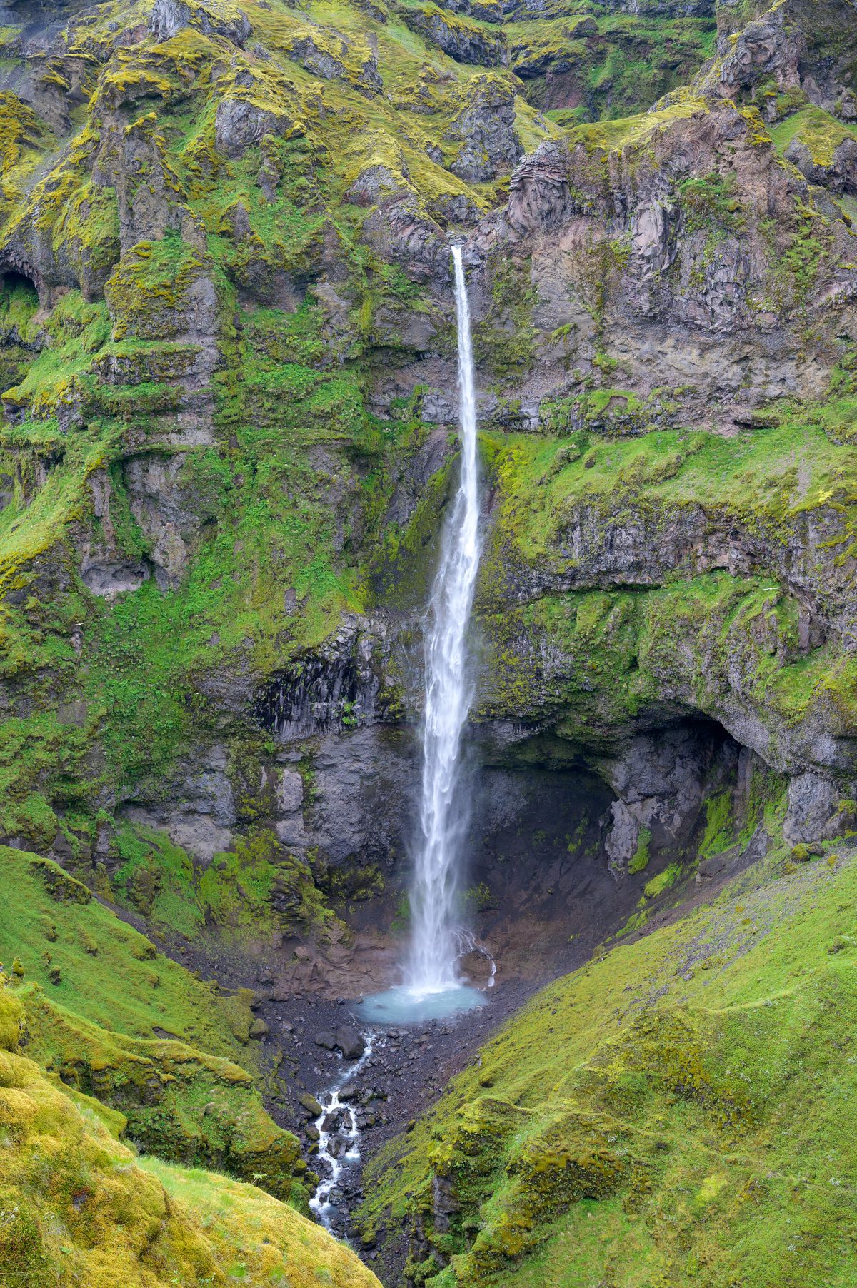 Hangandifoss plunges in a single white ribbon into a dark hollow surrounded by luminous green cliffs.
