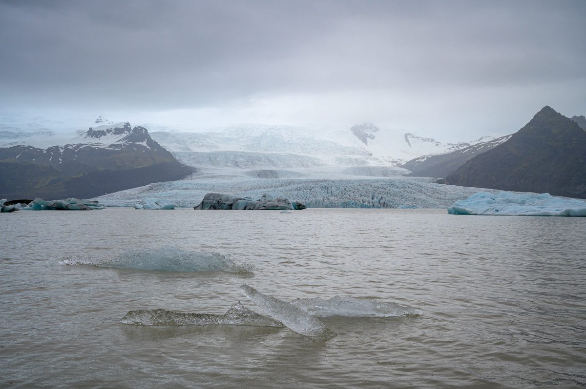 A glacier meets the steel-gray waters of Fjallsárlón beneath mist, rain, and low cloud.