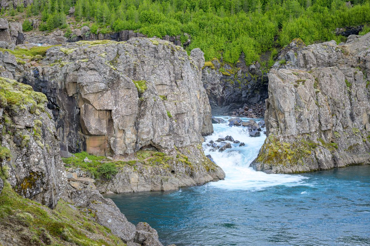 Turquoise water rushes between weathered basalt walls before settling into a deep pool.