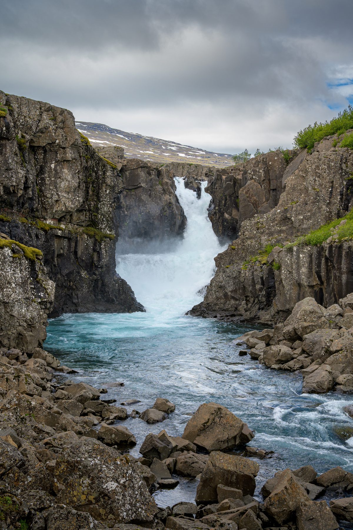 Sveinsstekksfoss plunges through a narrow basalt cleft into a cold blue pool below.