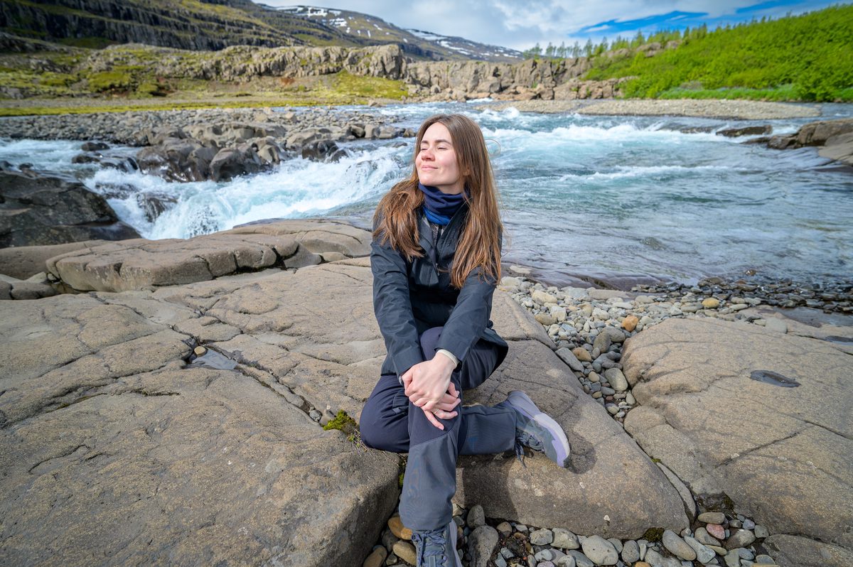 A traveler rests on smooth river rocks beside the rushing blue water of the Fossá.