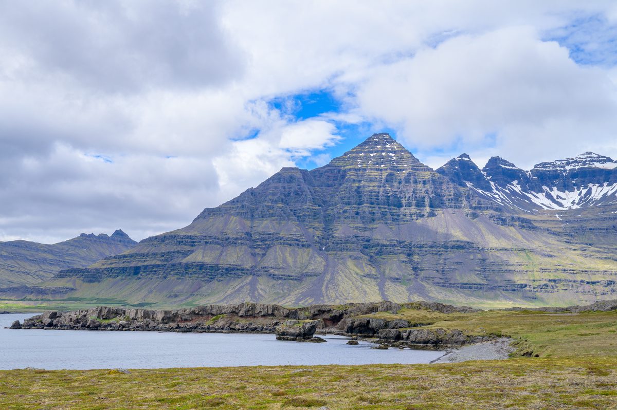 A sharply layered mountain rises over a quiet inlet, its upper ridges streaked with late snow.