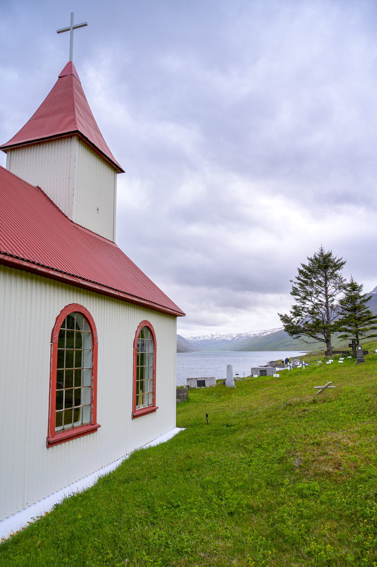 The white church with red trim overlooks a hillside cemetery and the long narrow fjord.