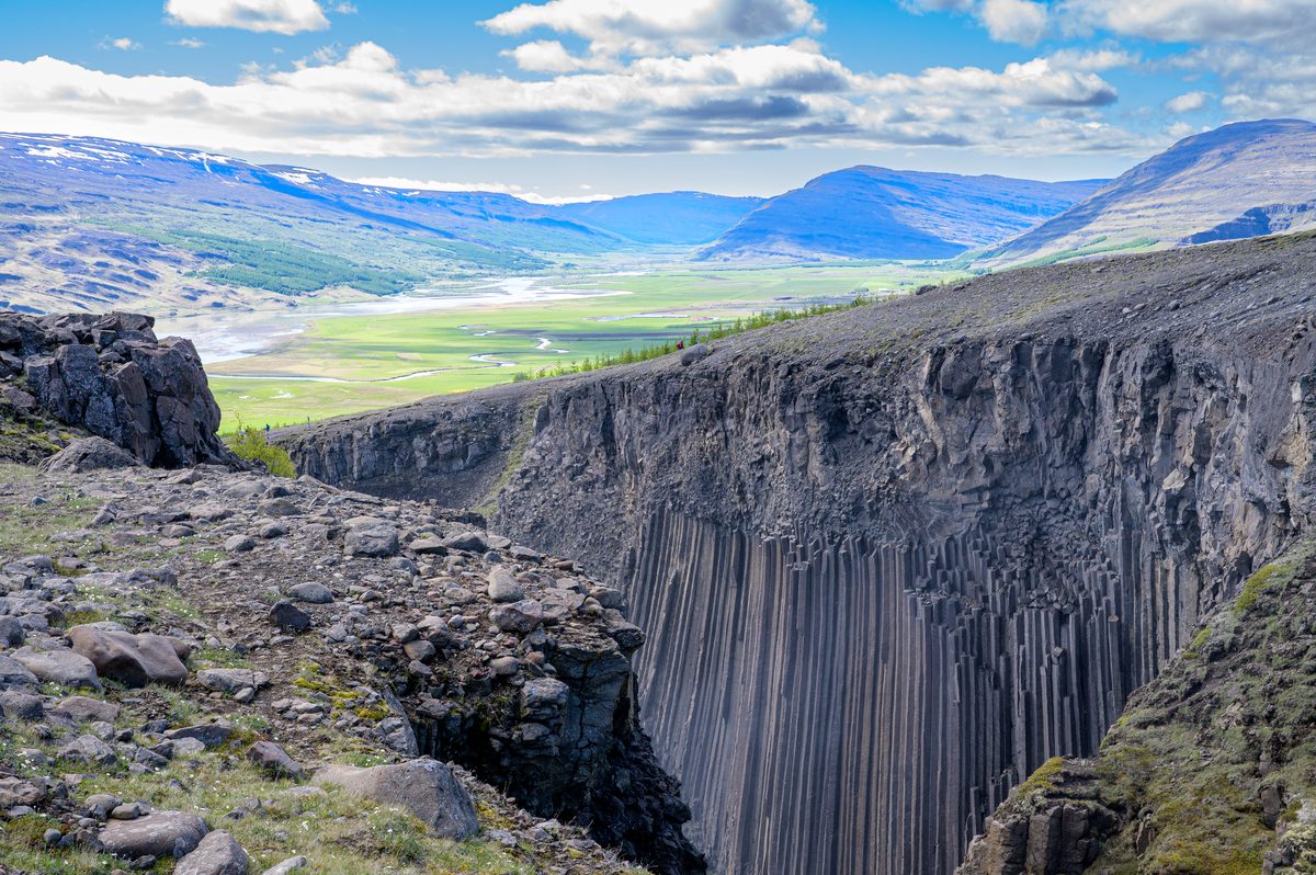 A dramatic wall of vertical basalt columns forms the edge of a deep river gorge beneath open highland views.