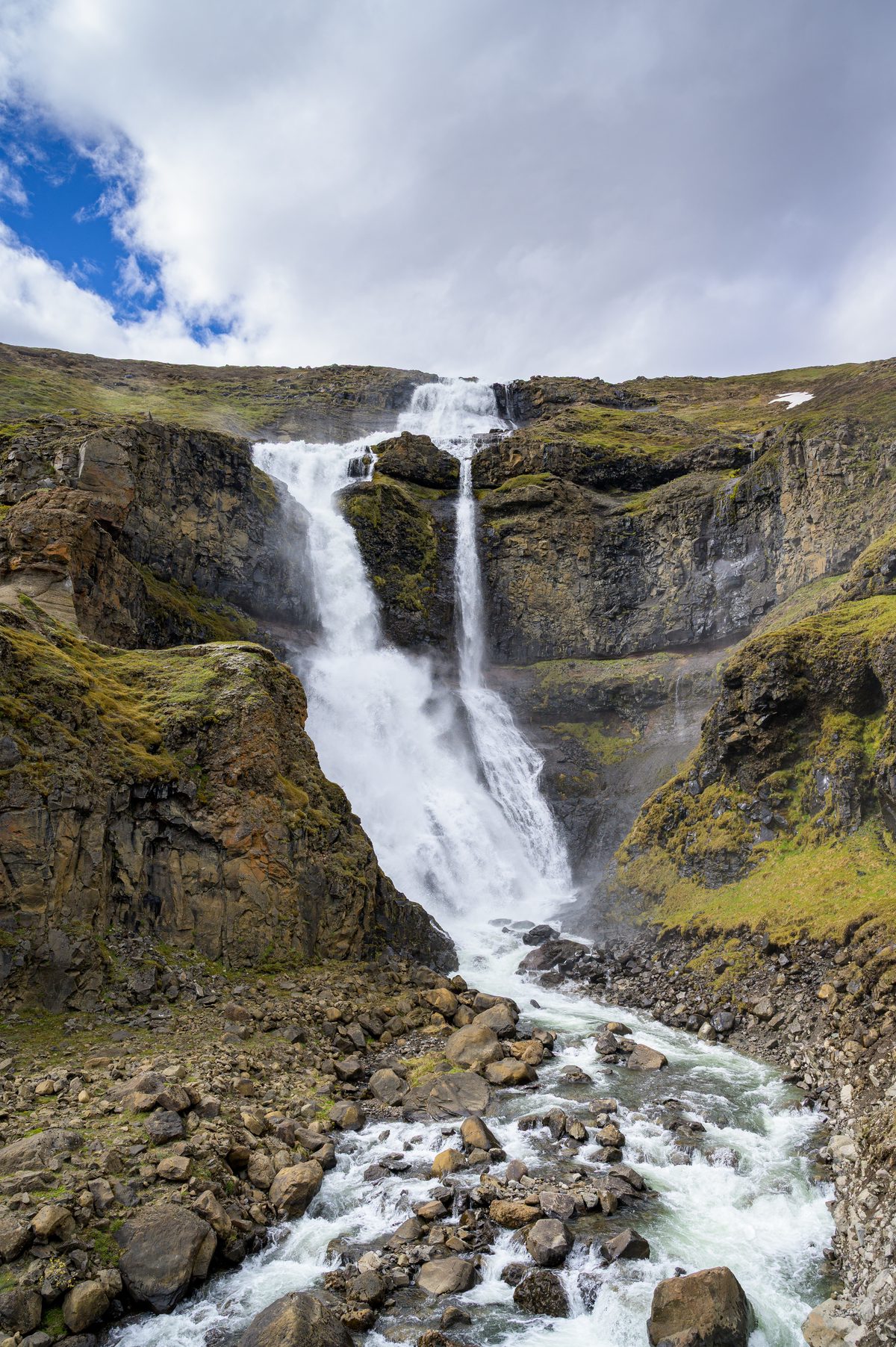 A white cascade tumbles down a dark mossy gully beside the mountain road above Seyðisfjörður.