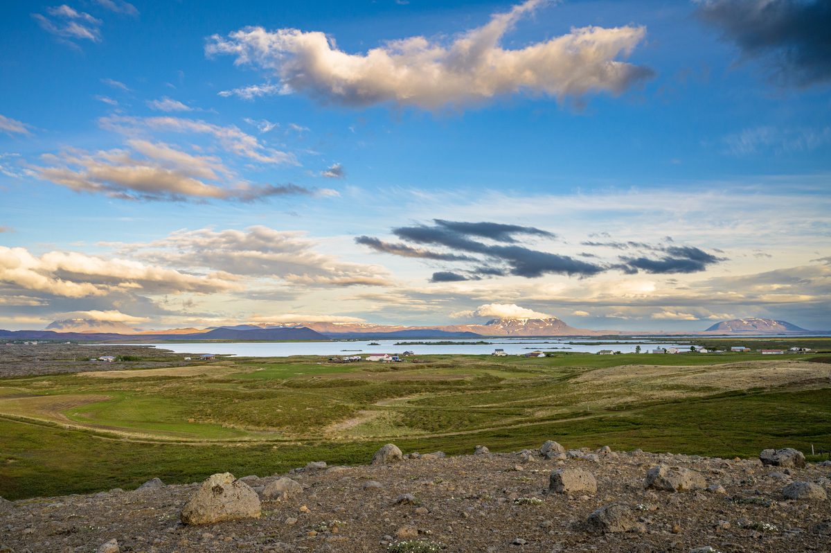 A wide green plain dotted with water stretches toward low mountains beneath softly lit evening clouds.