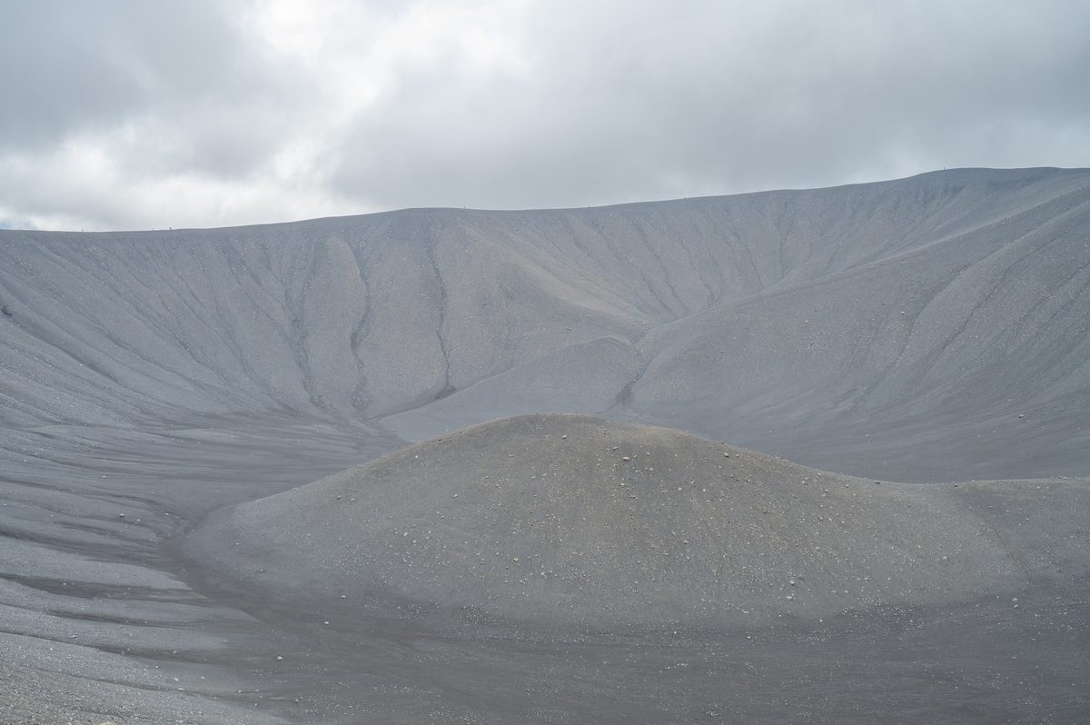 Fine erosion lines descend the steep gray walls of Hverfjall toward a rounded mound on the crater floor.