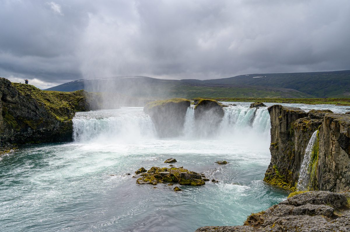 Powerful white water pours over the curved basalt ledges of Goðafoss, sending mist into the dark cloudy air.