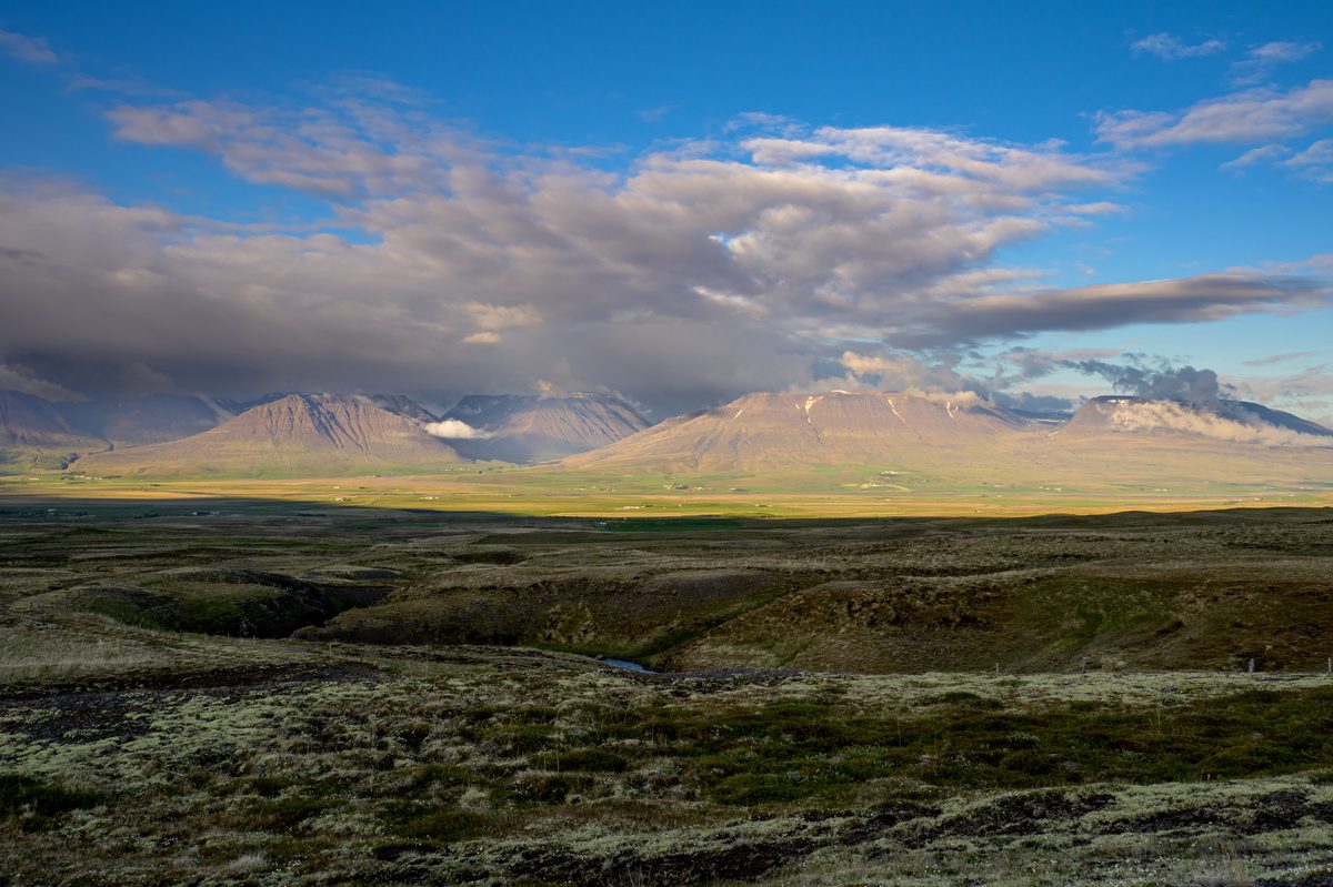 Long low sunlight warms a broad Skagafjörður mountain ridge beyond mossy ground and shallow winding gullies.